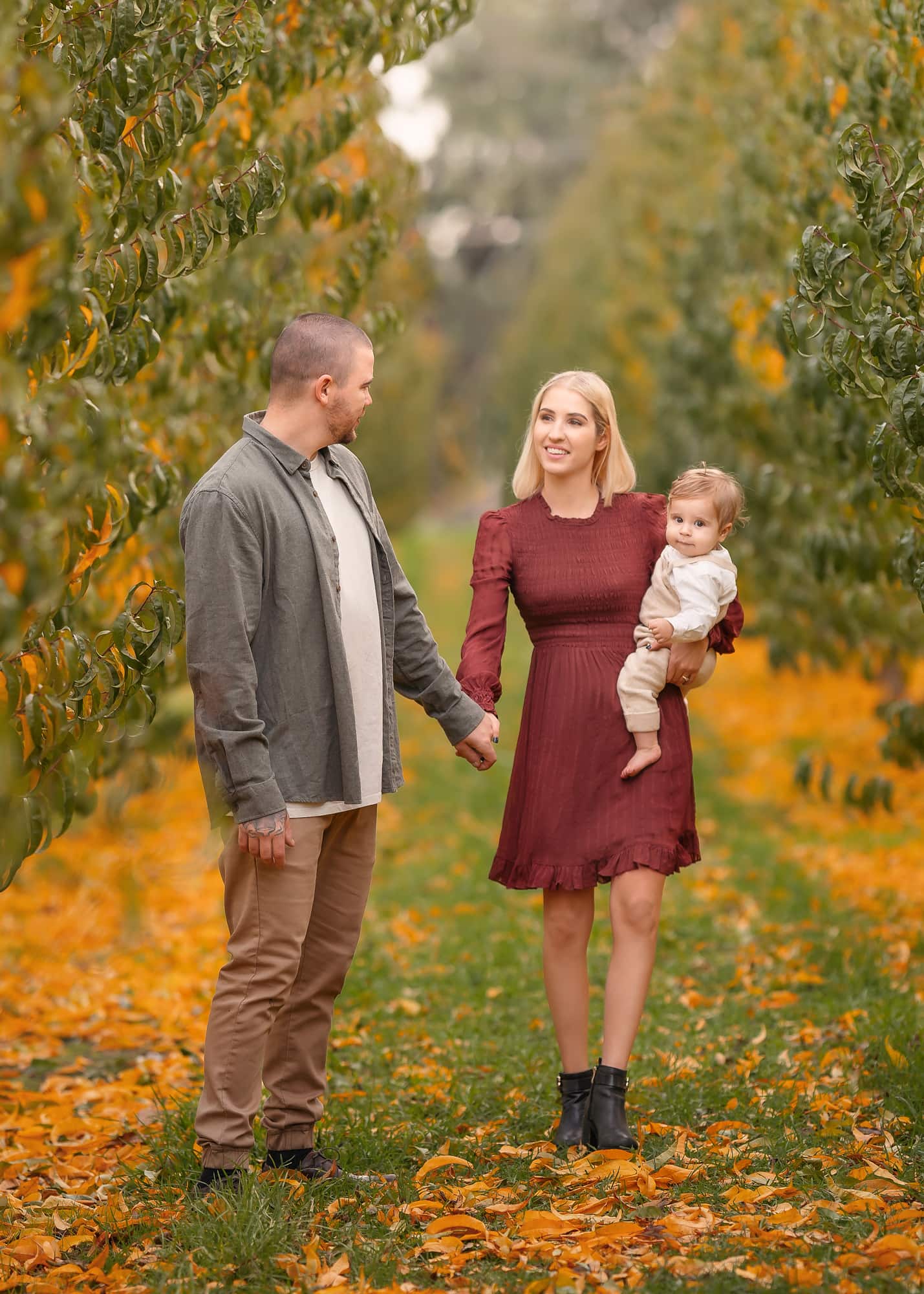 Perth parents with baby walking in an orchard during autumn family portrait session.